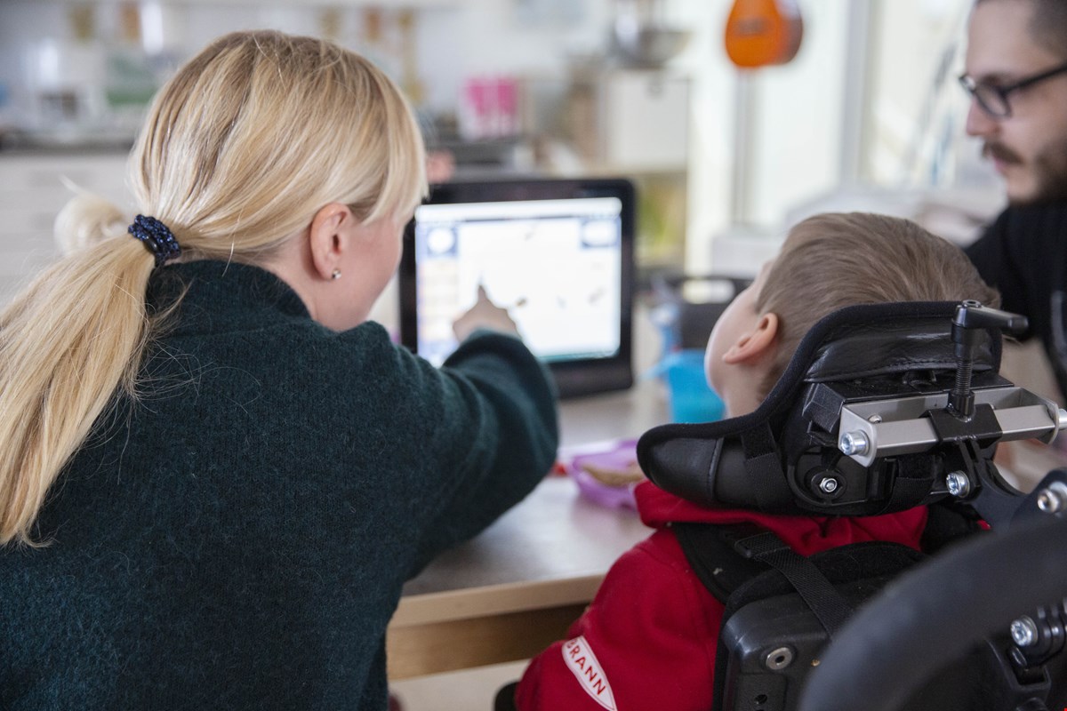 Bildet viser bakhodet til Torbjørn og assistenten Linda. Linda har langt lyst hår i hestehale og Torbjørn har kort brunt hår. Linda peker på Tobii-skjermen som er uklar foran dem.